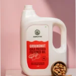 Amrutva Cold Pressed Groundnut Oil - A bottle of groundnut oil beside a bowl of peanuts.