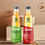 Amrutva Cold Pressed Groundnut and Sesame Oil Combo. This image shows two bottles of cold pressed oil; one groundnut and one sesame; alongside raw ingredients.