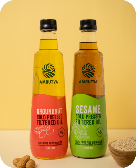 Amrutva Cold Pressed Groundnut and Sesame Oil Combo. This image shows two bottles of cold pressed oil; one groundnut and one sesame; alongside raw ingredients.