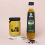 black sesame oil and black tahini with some black sesame seeds sprinkled around the bottles as its made by sesame seeds black