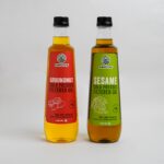 Amrutva Cold Pressed Groundnut and Sesame Oil Combo. This image shows two bottles of cold pressed oil; one groundnut and one sesame; alongside raw ingredients.