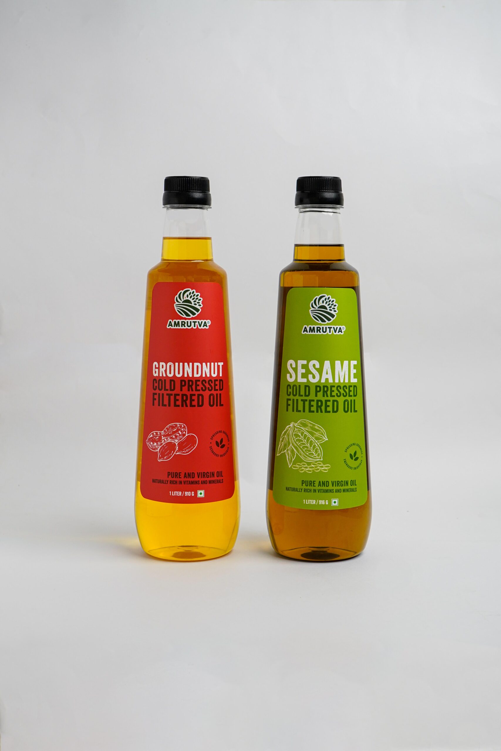 Amrutva Cold Pressed Groundnut and Sesame Oil Combo. This image shows two bottles of cold pressed oil; one groundnut and one sesame; alongside raw ingredients.